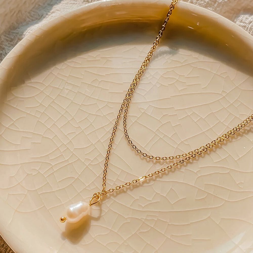 Gold layered necklace with freshwater pearl pendant displayed on ceramic plate.