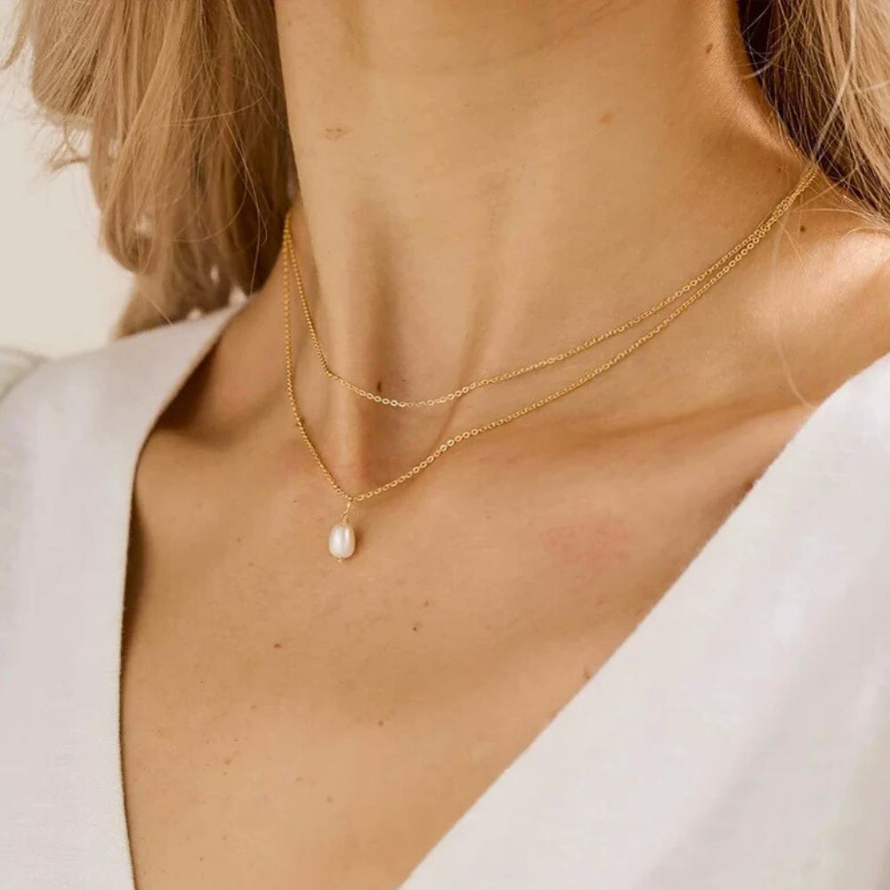 Gold layered pearl necklace worn by model in natural light close-up.