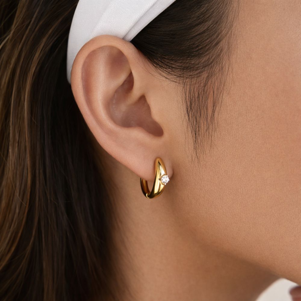 Minimalist gold huggie hoop earrings with white zircon worn by woman