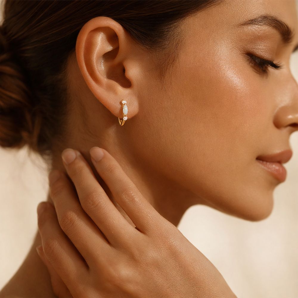 Close-up of gold opal huggie earrings worn on ear with oval opal stone and zircon accents
