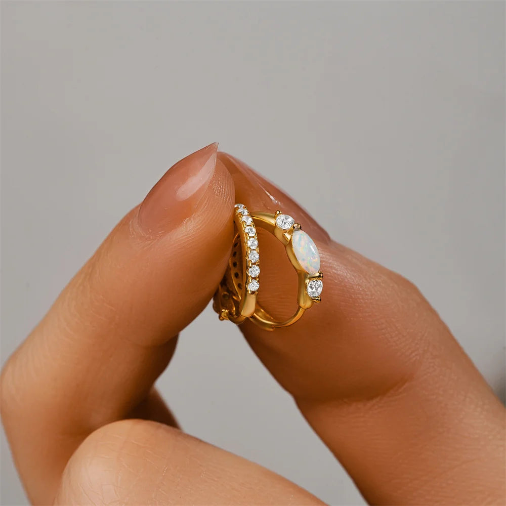 Small gold opal huggie earrings held between fingers showing scale and details