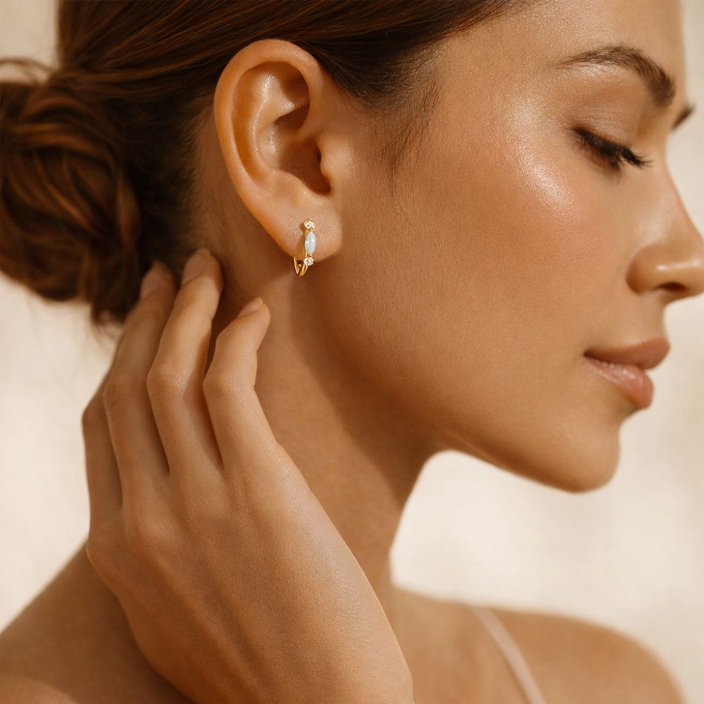 Woman wearing gold opal huggie hoop earrings in 925 sterling silver gold plated finish