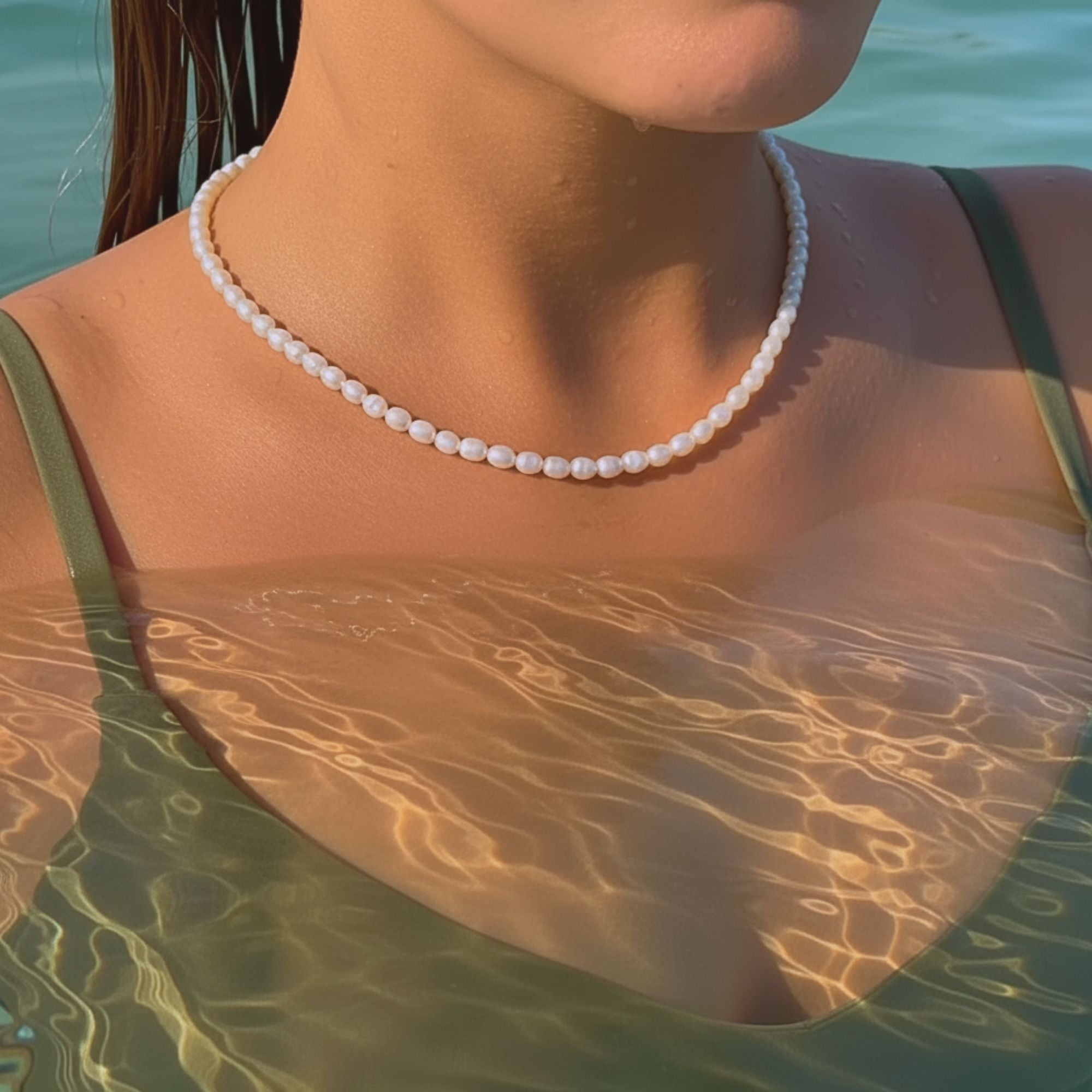 
A Caucasian woman wearing the Beach Bloom Jewelry pearl necklace in the sea