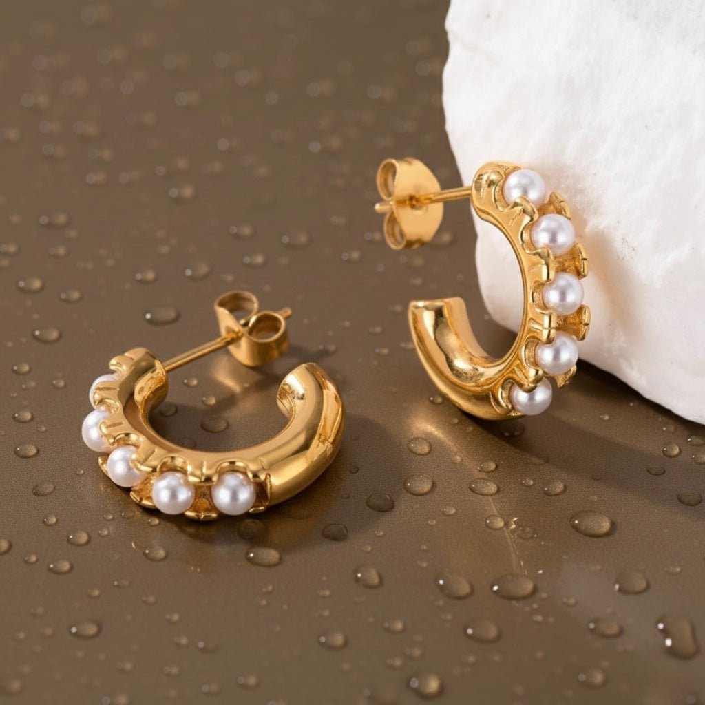 Gold pearl huggie earrings photographed on brown background with water drops, waterproof jewelry design