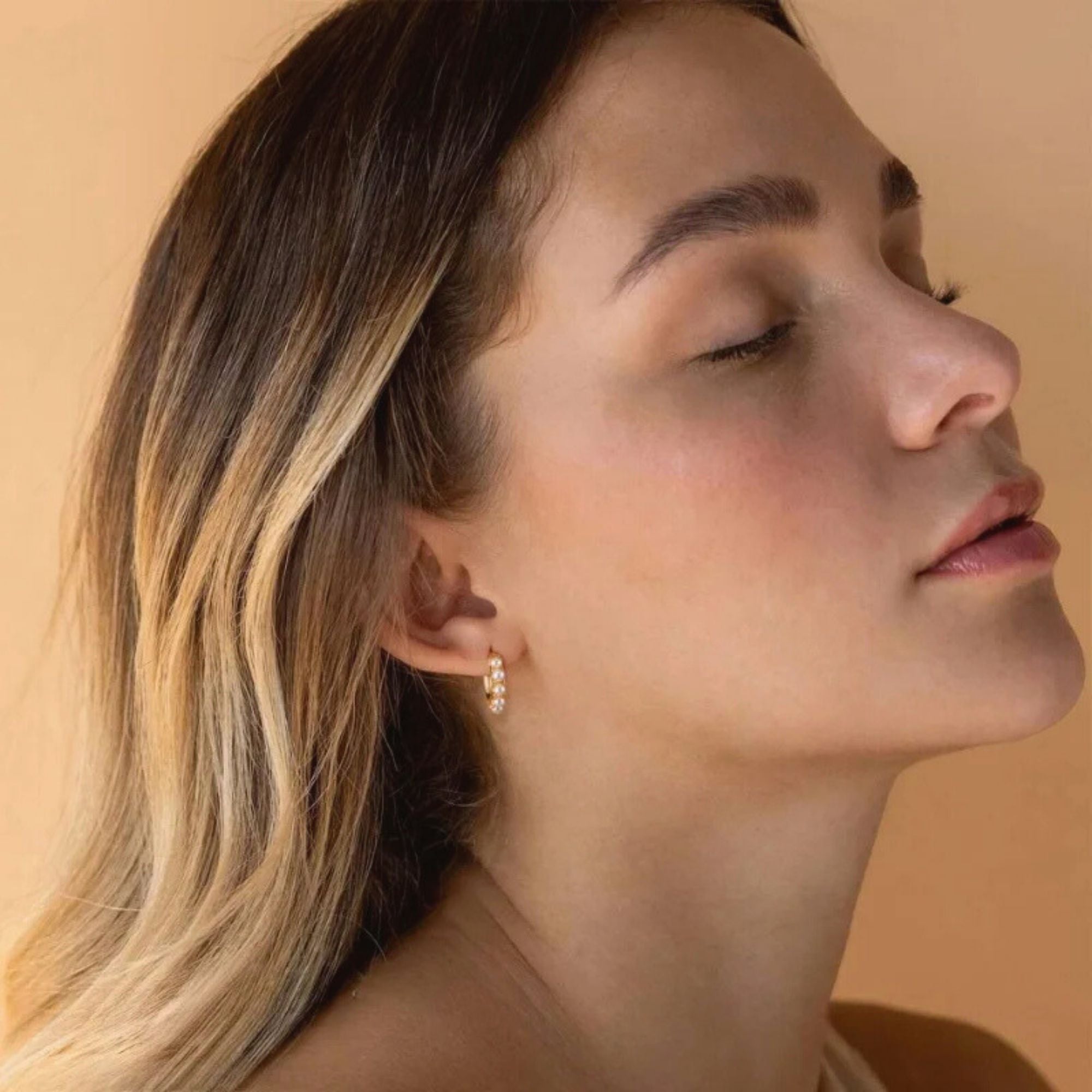 Woman wearing gold pearl huggie earrings, elegant dainty waterproof jewelry for everyday wear