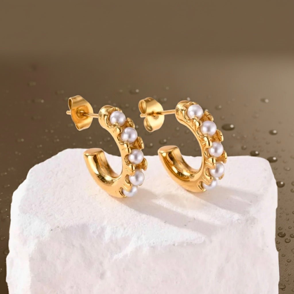 Gold pearl huggie earrings displayed on white stone, 18K gold-plated hoops with freshwater pearls and waterproof finish