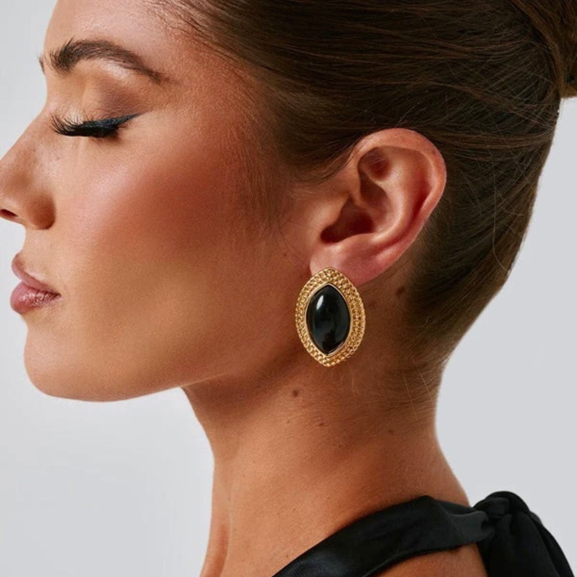 Close-up of retro marquise earrings with twisted gold frame and glossy black stone