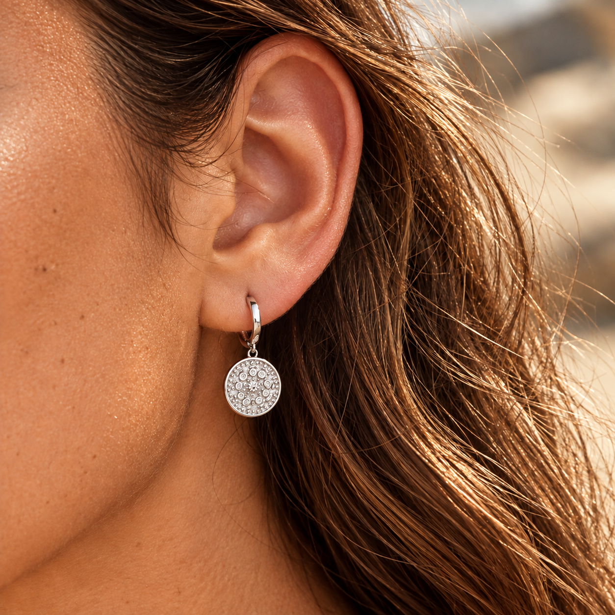 Close-up of a brunette wearing silver round charm hoop earrings with an ornate medallion pendant