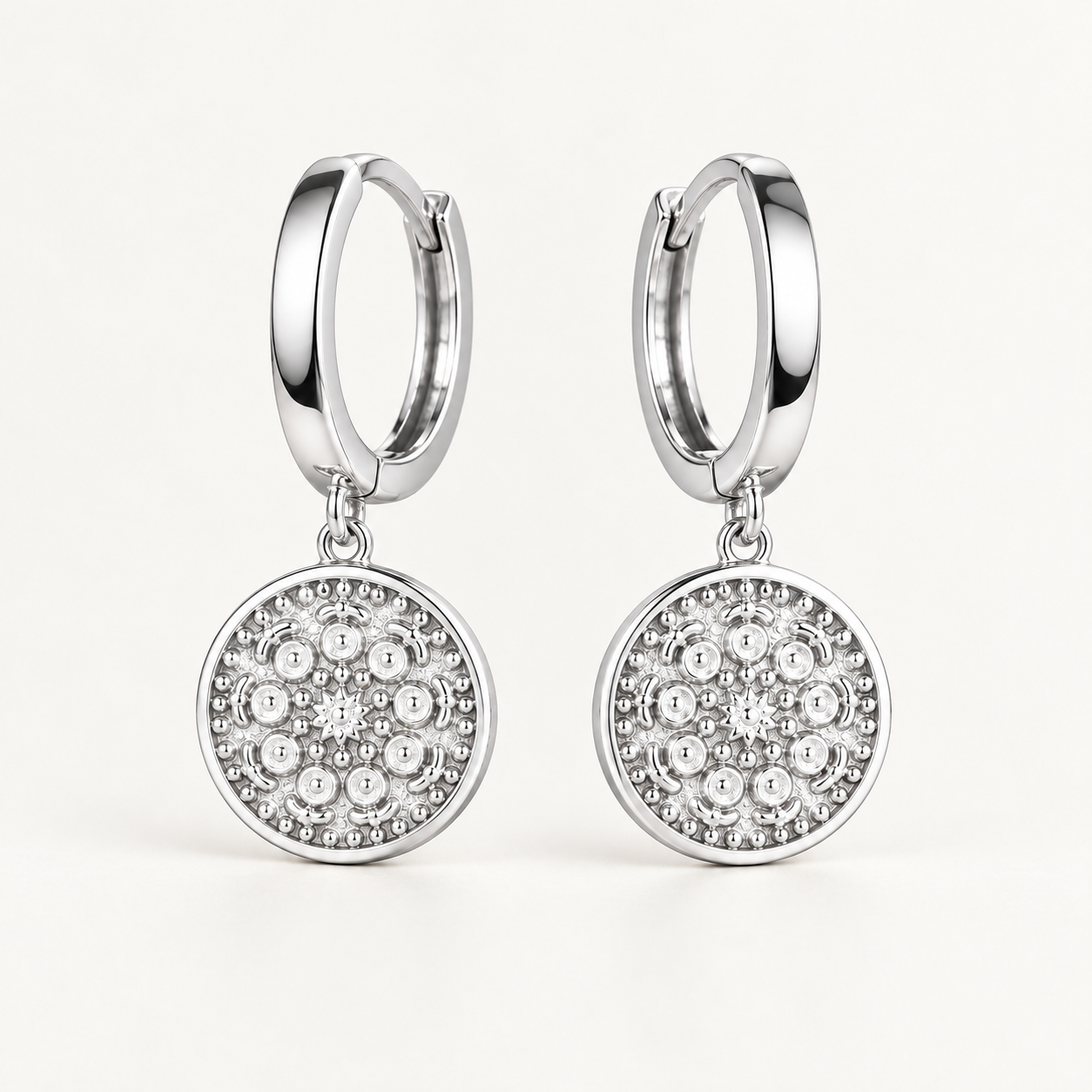 Pair of 925 sterling silver hoop earrings with textured round medallion charms on an ivory background
