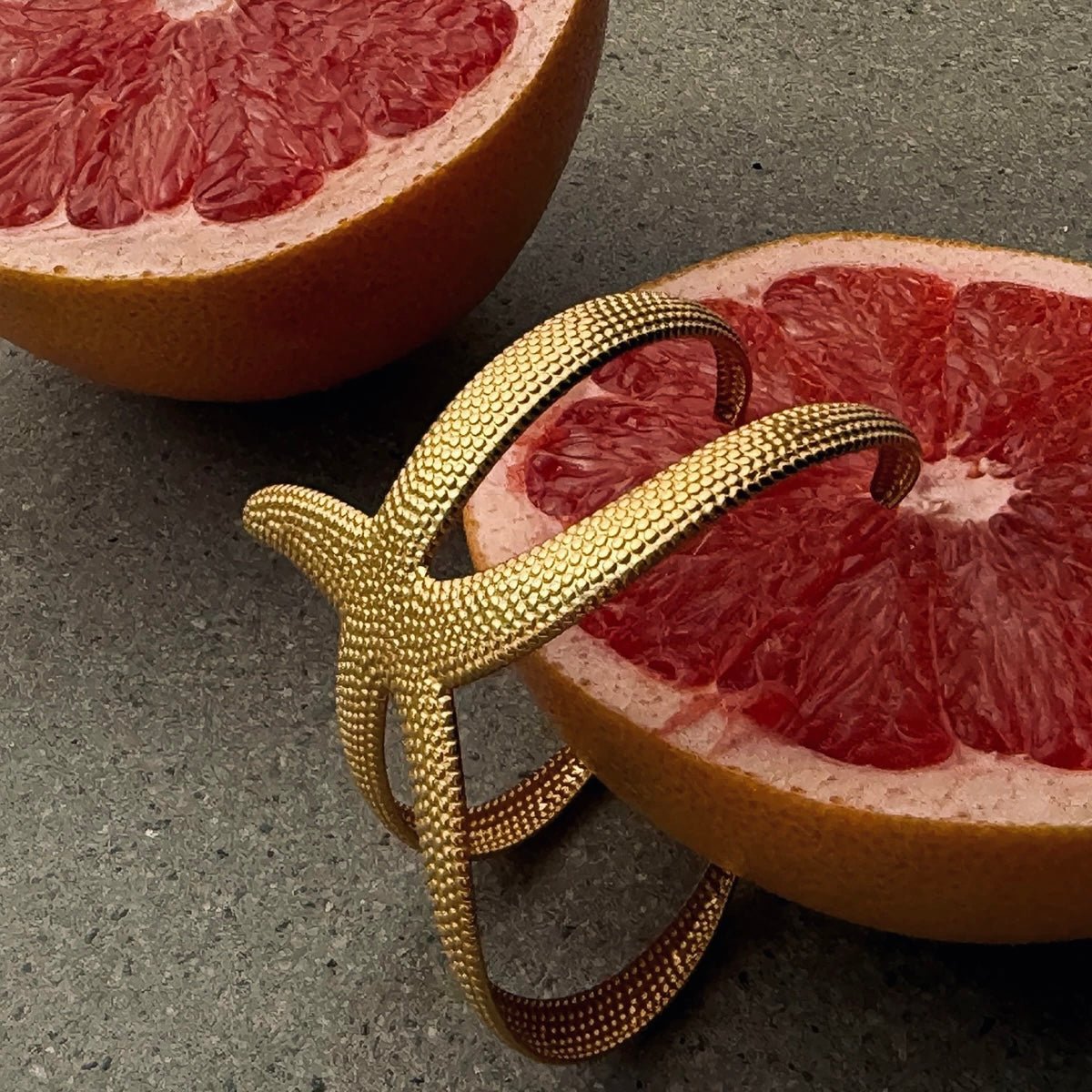 Gold starfish bracelet in a bold flatlay with grapefruit halves