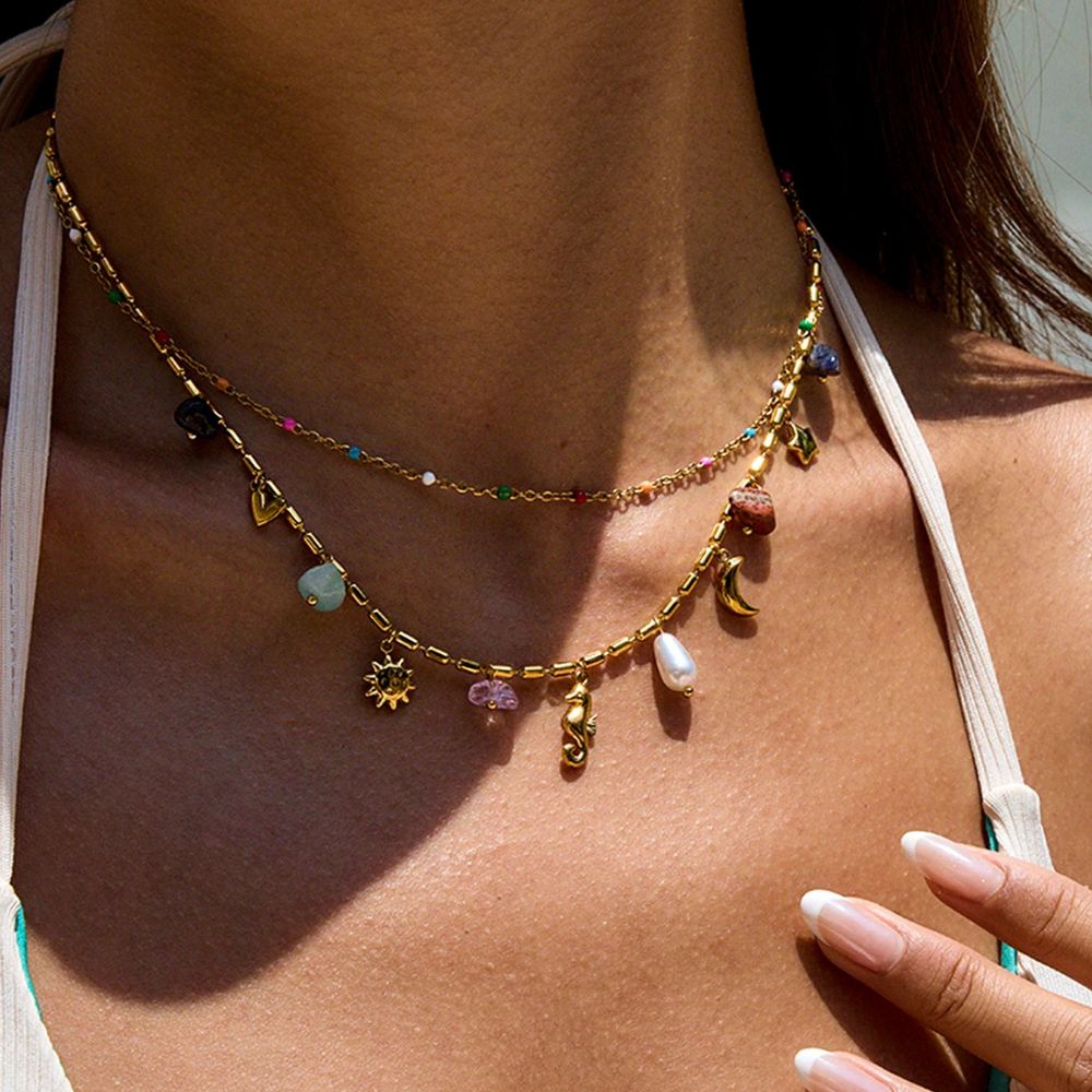 Layered gold necklace with charms and beads worn in sunlight, summer beach look