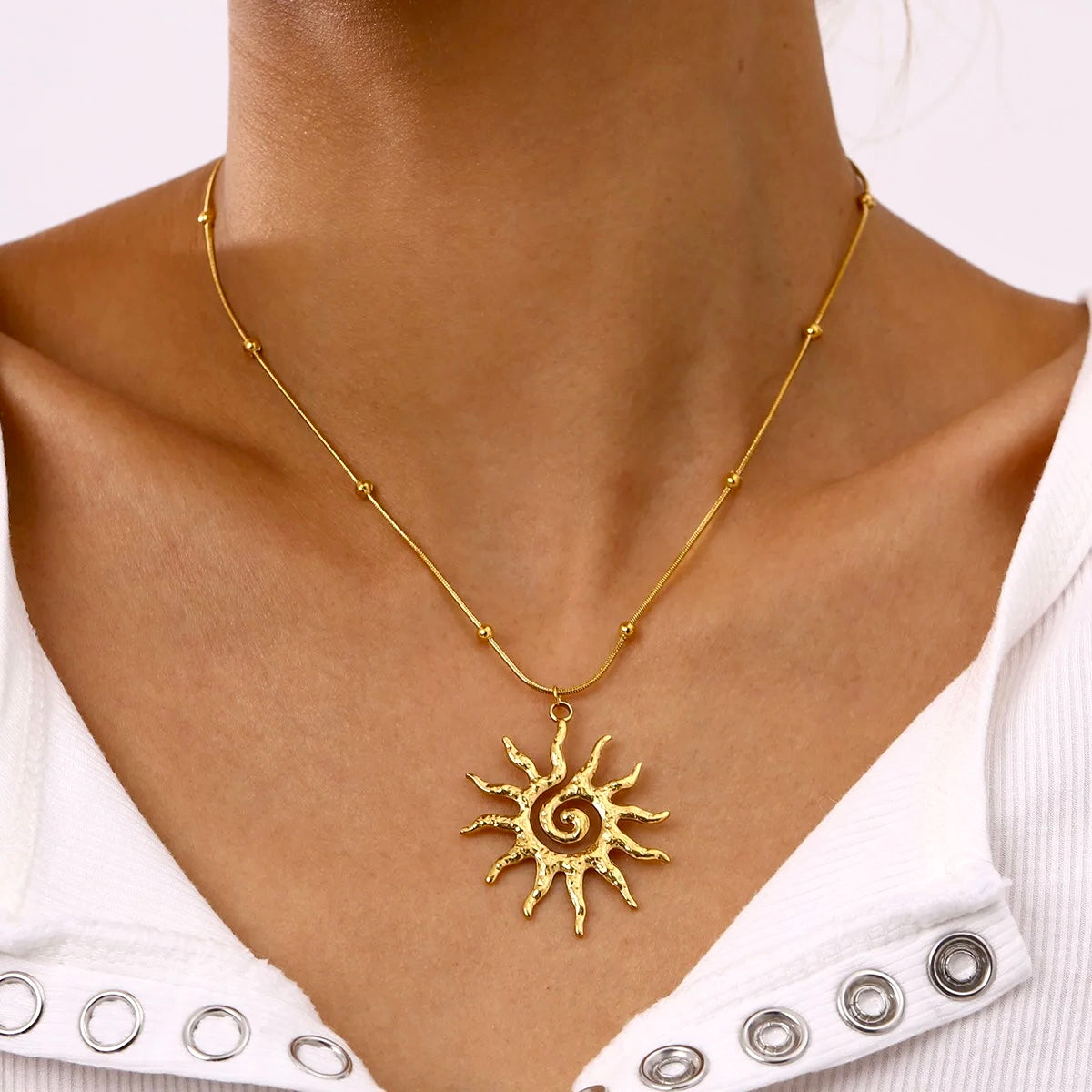 Close-up of gold sun necklace worn with an open white shirt