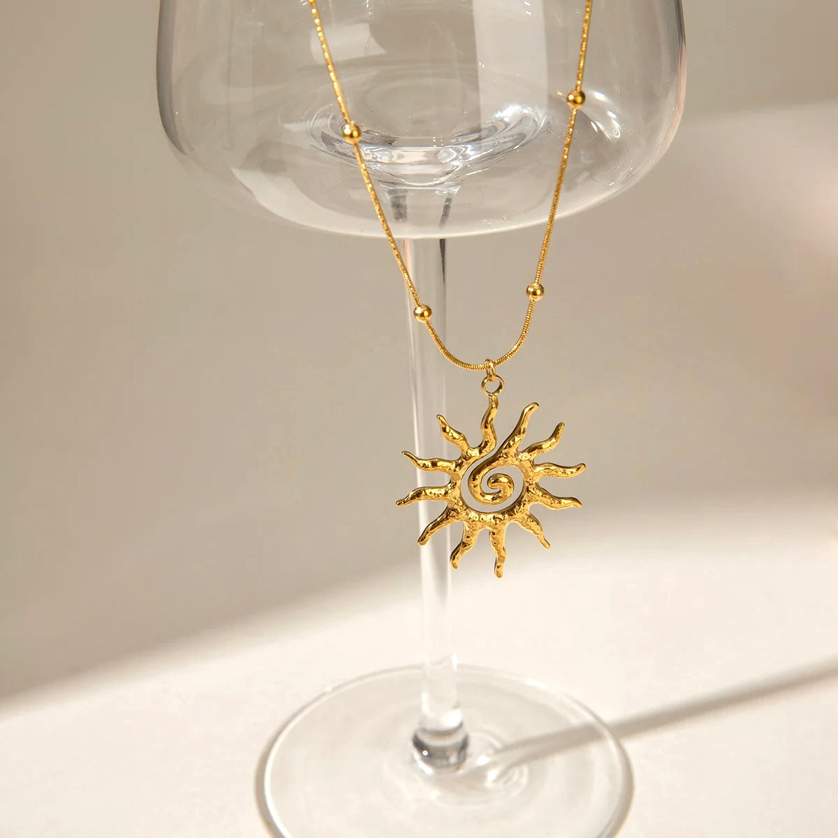 Gold sun pendant necklace displayed elegantly on a glass stem