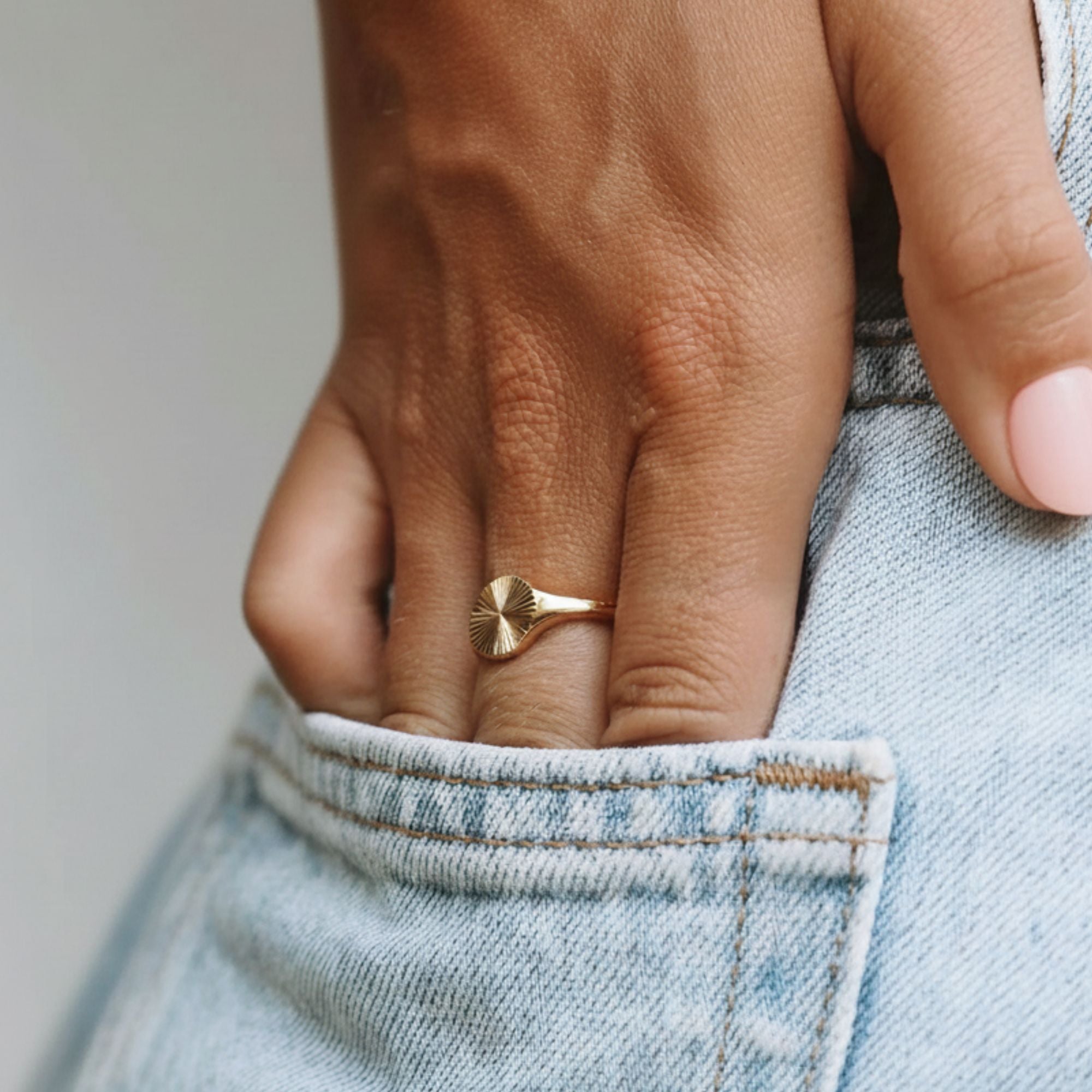 Hand wearing the Sunbeam Gold Signet Ring with jeans – minimalist waterproof gold jewelry by Beach Bloom Jewelry.