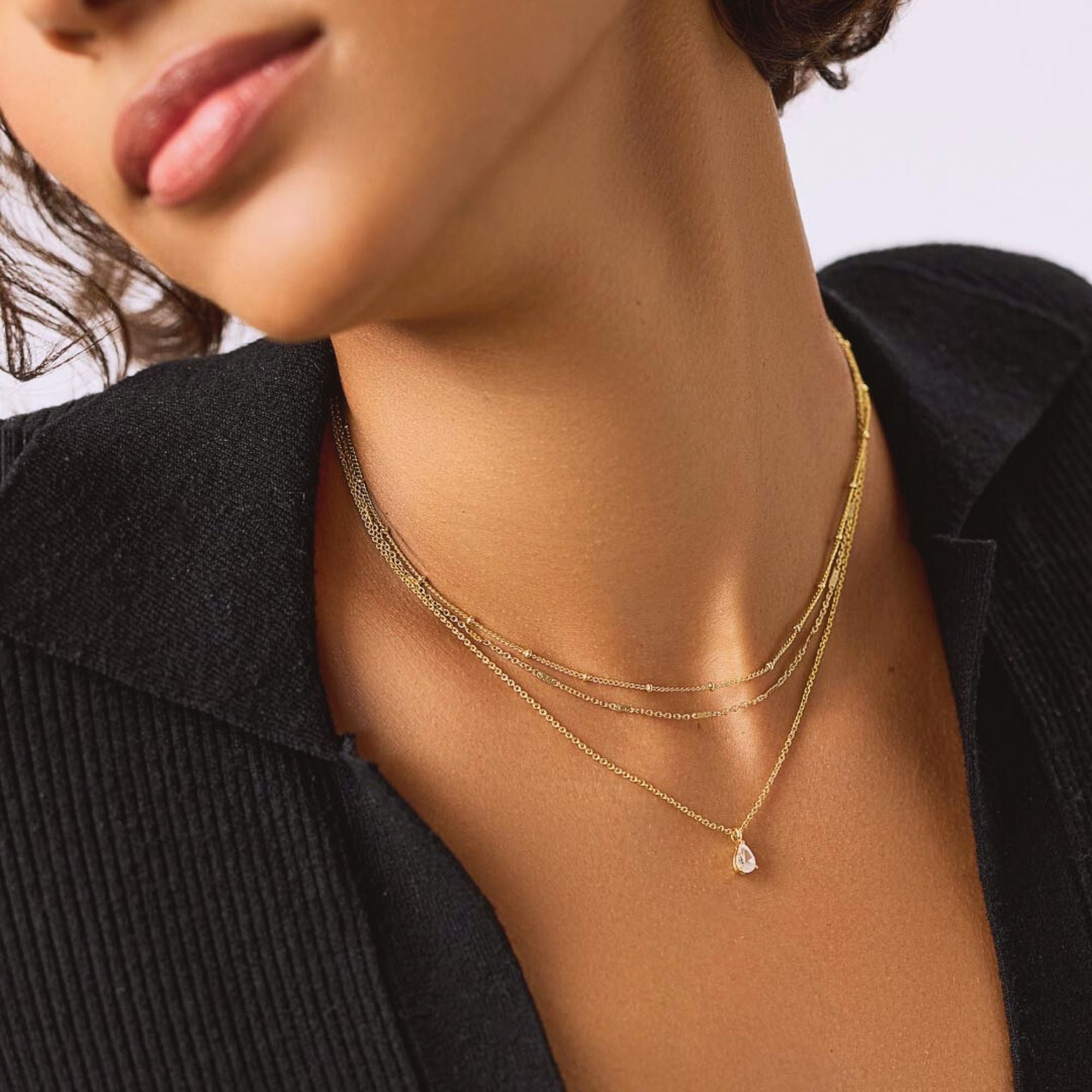 Talia layered gold necklace with three delicate chains and teardrop pendant worn around the neck.