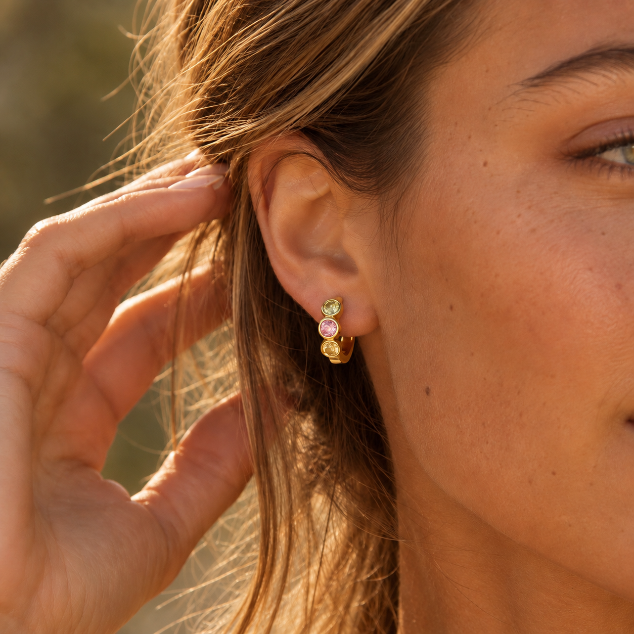 Chunky gold huggie earring with three colorful zirconia stones worn on ear