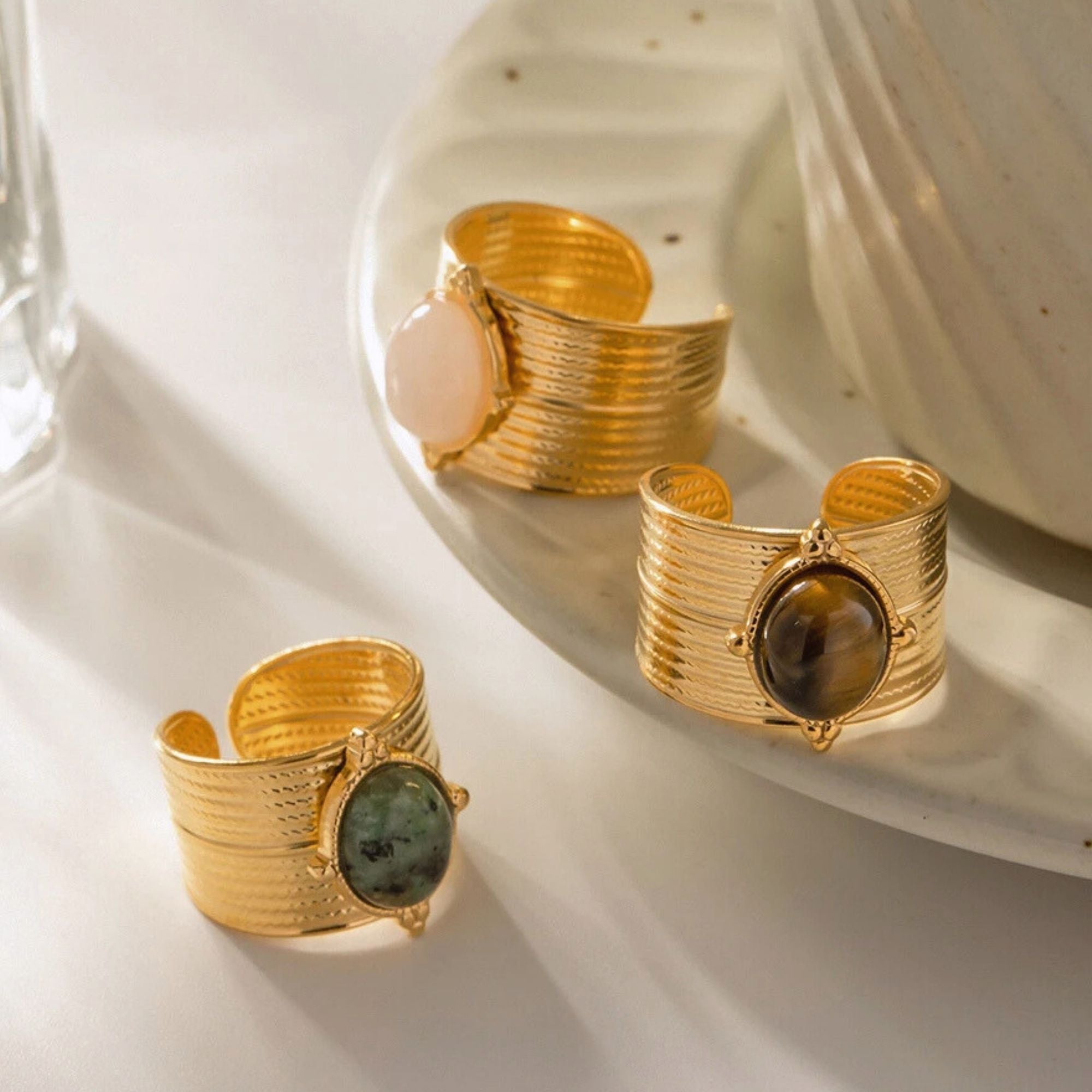 Wide band gold gemstone rings with Rose Quartz, Tiger’s Eye, and Green Jasper on display