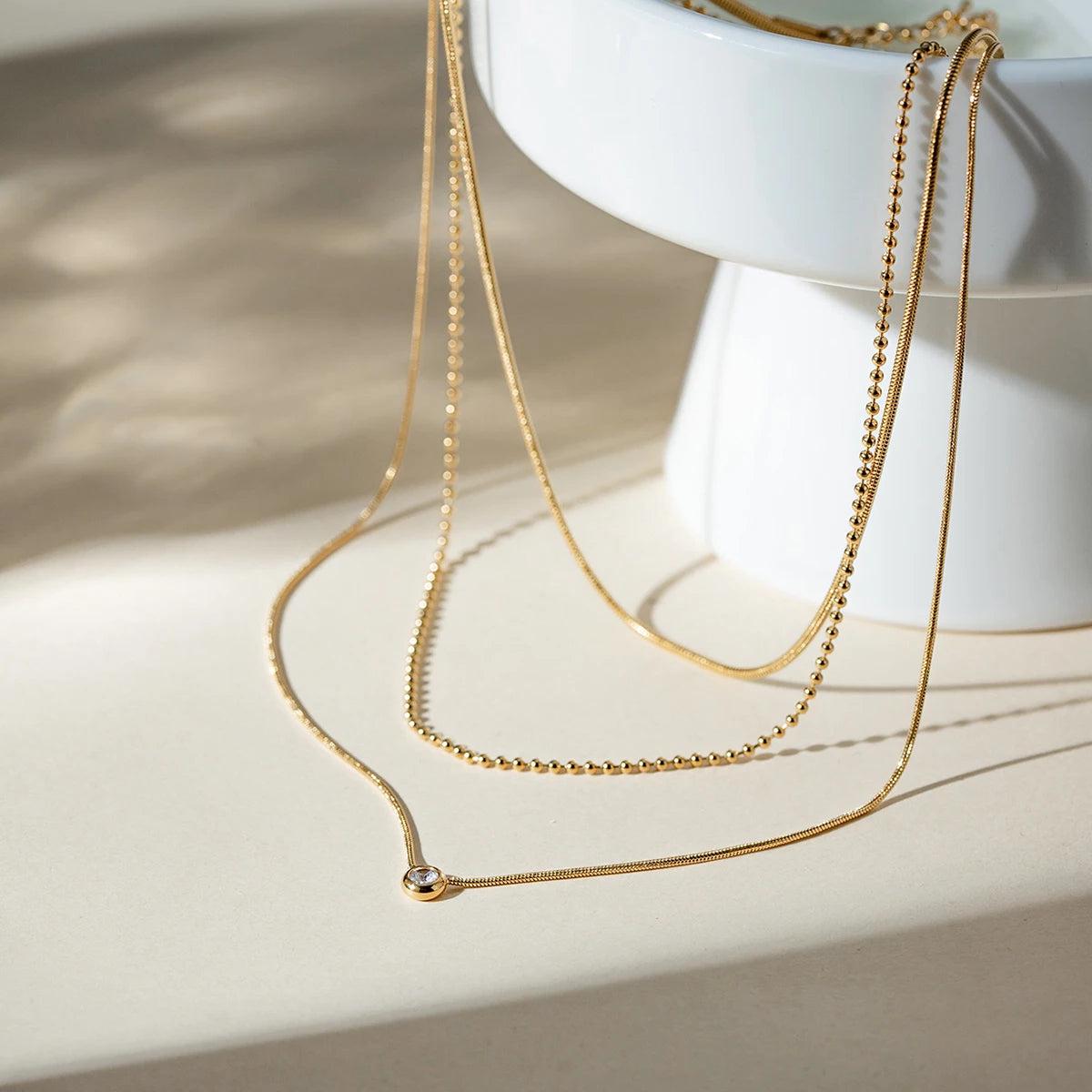 Zahia layered gold necklace with a solitaire pendant styled on a white bowl.