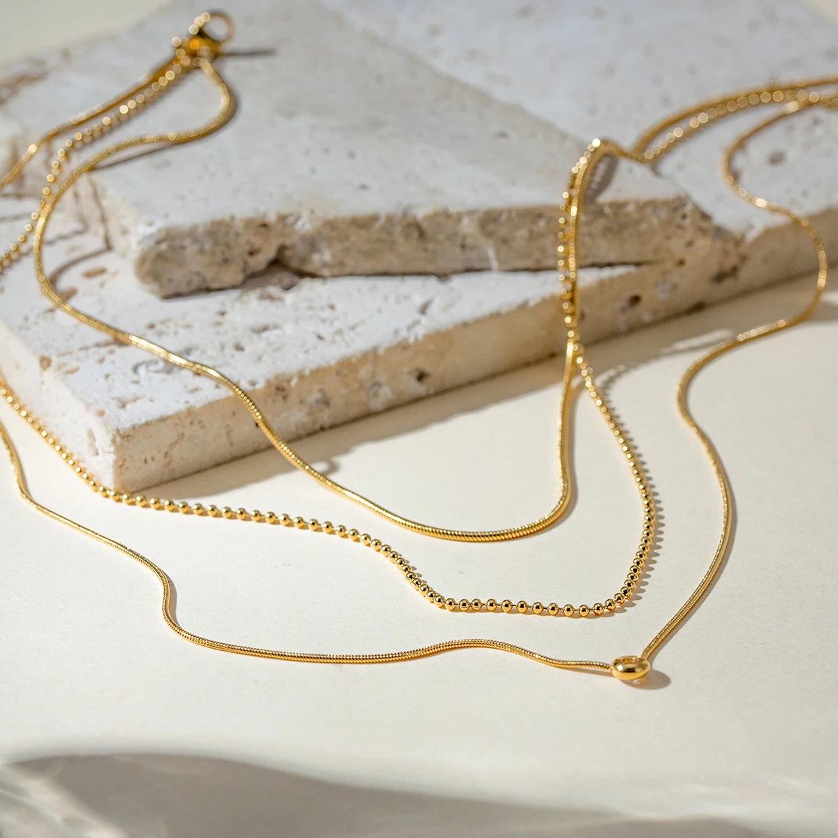 Zahia layered necklace with dainty chains and solitaire pendant laid on textured stone.